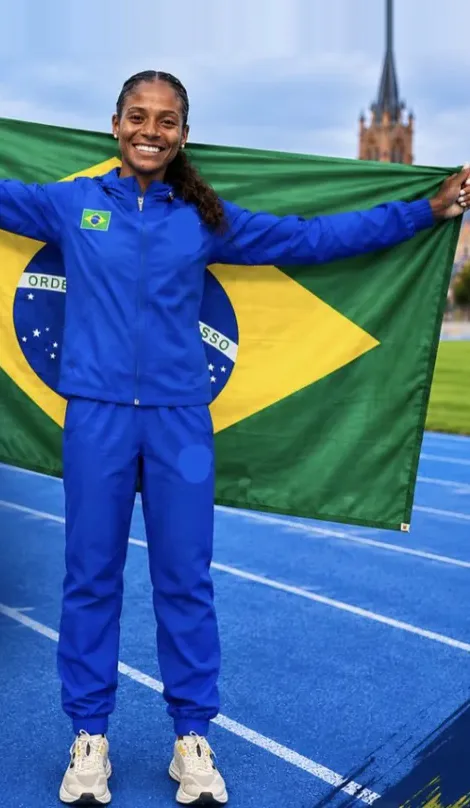 Jéssica sorri segurando a bandeira do Brasil na pista, no Mundial de Copenhague